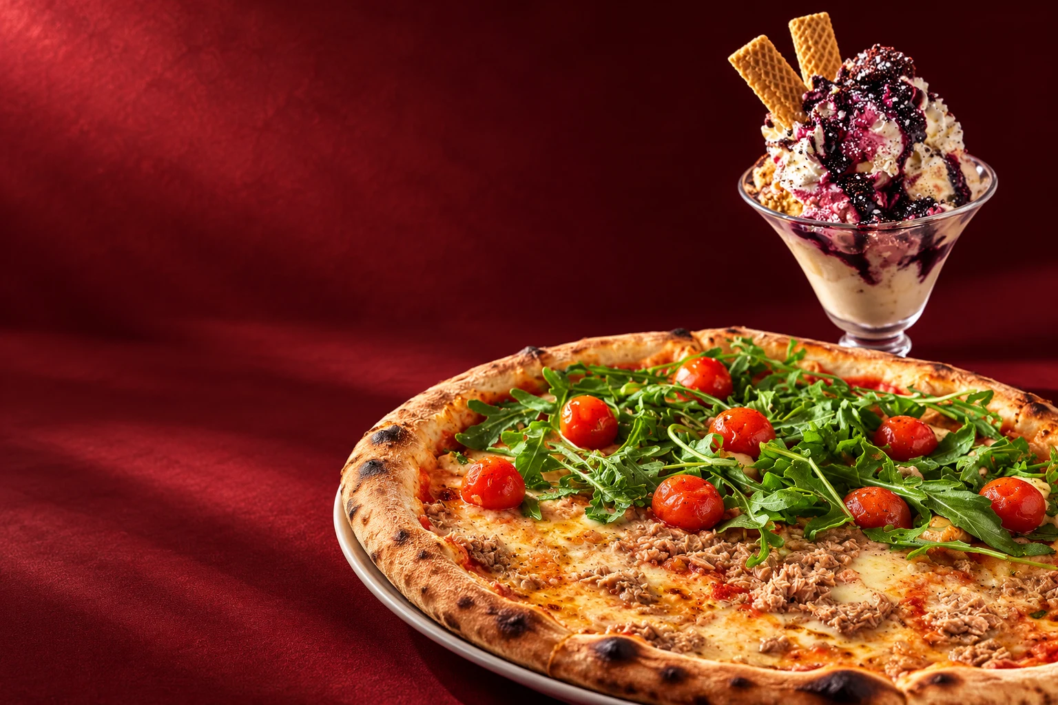 Künstlerische Food-Inszenierung von Pizza und Eisbecher auf bordeauxrotem Hintergrund
